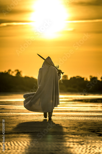 Portrait of assassin in white costume with the sword at the sea. He is posing...