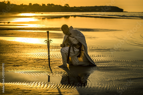 Portrait of assassin in white costume with the sword at the sea. He is posing...