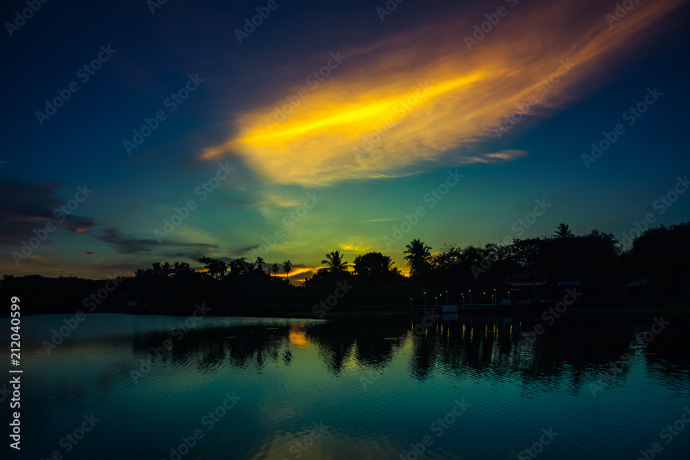 Colorful sky sunset with cloud above silhouettes of trees at riverside.