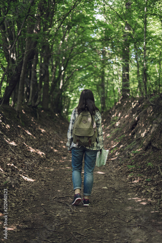 Young woman with backpack explores map on forest path. Woman with tourist backpack travels