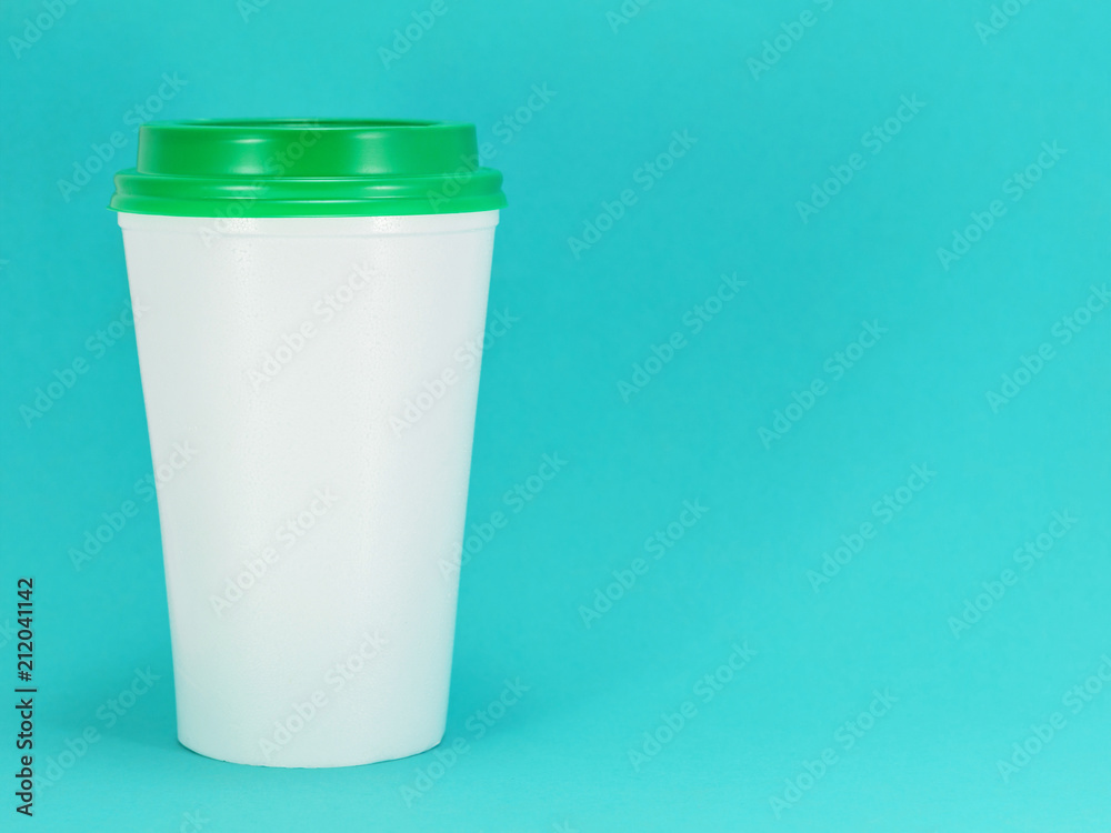 white plastic coffee cup with green lid on a blue background, front view with copy space
