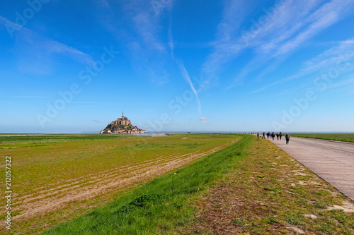 Road to amazing Mont Saint Michel abbey. Tourists are going to the abbey. It is one of the most famous tourist attractions in France. Landscape photo during sunrise. Normandy, France
