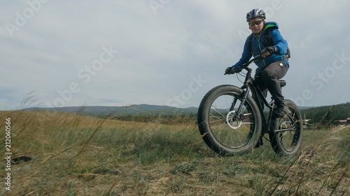 Fat bike also called fatbike or fat-tire bike in summer driving through the hills. The guy is riding a bike along the sand and grass high in the mountains. He performs some tricks and runs dangerously