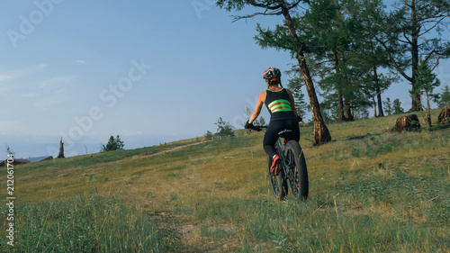Fat bike also called fatbike or fat-tire bike in summer riding in the forest. Beautiful girl and her bicycle in the forest. She rolls her bike and poses to the operator. © ivandanru