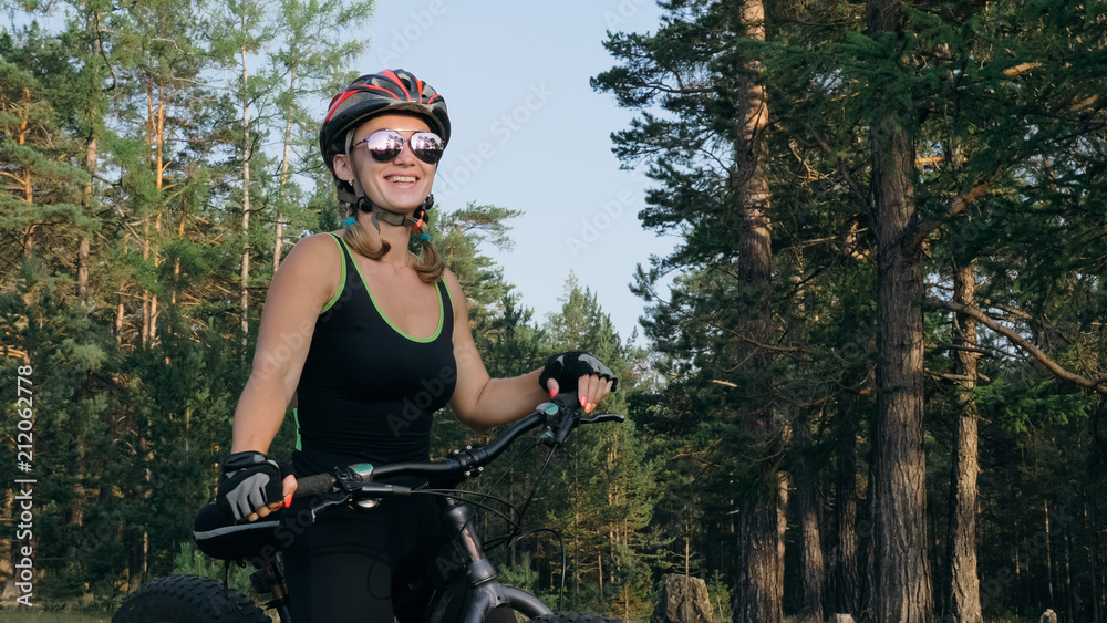 Fat bike also called fatbike or fat-tire bike in summer riding in the forest. Beautiful girl and her bicycle in the forest. She poses and smiles to the operator. Very positive and provocative. Fat bike also called fatbike or fat-tire bike in summer riding in the forest. Beautiful girl and her bicycle in the forest. She poses and smiles to the operator. Very positive and provocative.
