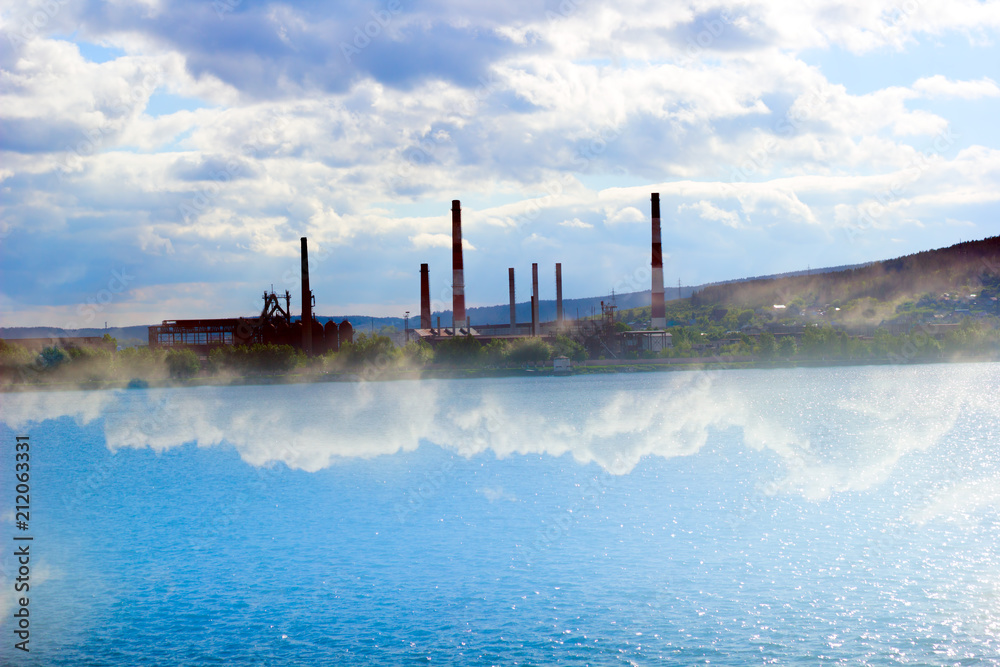 tubes of factory on a background of water and sky, environmental pollution concept