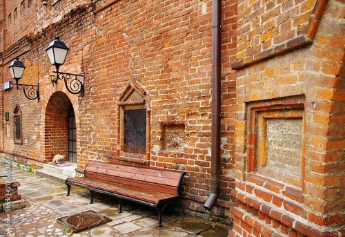 Fototapeta Naklejka Na Ścianę i Meble -  An ancient church building with a brick wall shop and street lamps over the door