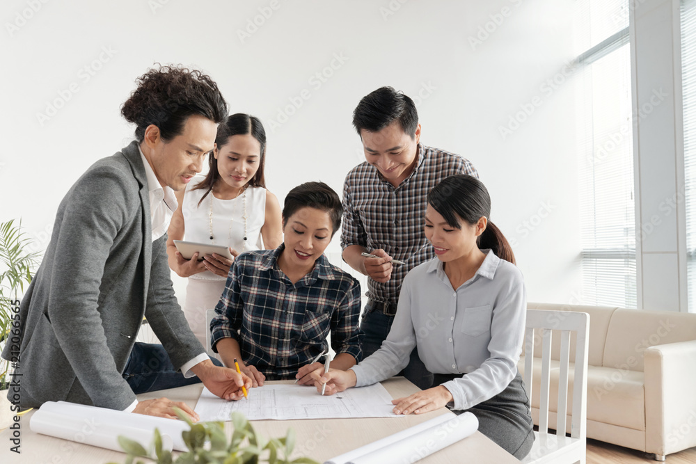 Group of architects working on blueprints together during a meeting Group of architects working on blueprints together during a meeting