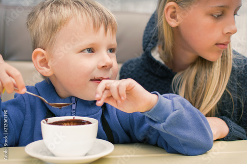 A small boy of 3-5 years old eats hot chocolate in a cafe, restaurant.