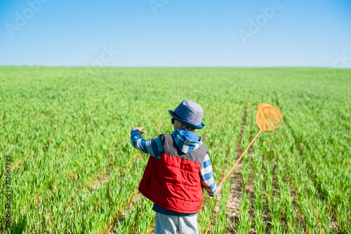 Little boy with a butterfly net in hand runs across the green field. photo