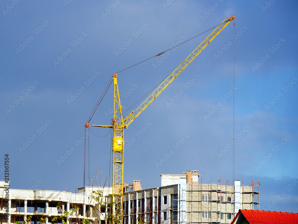 Crane near building. Building under construction. Construction site against blue sky.