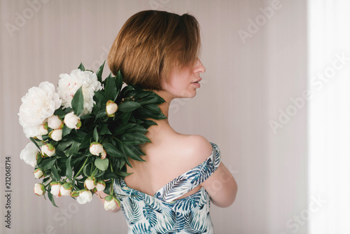 Young woman in fashon dress holding bouquet of beautiful white peonies flowers behind her back St. Valentine's Day, International Women's Day concept.