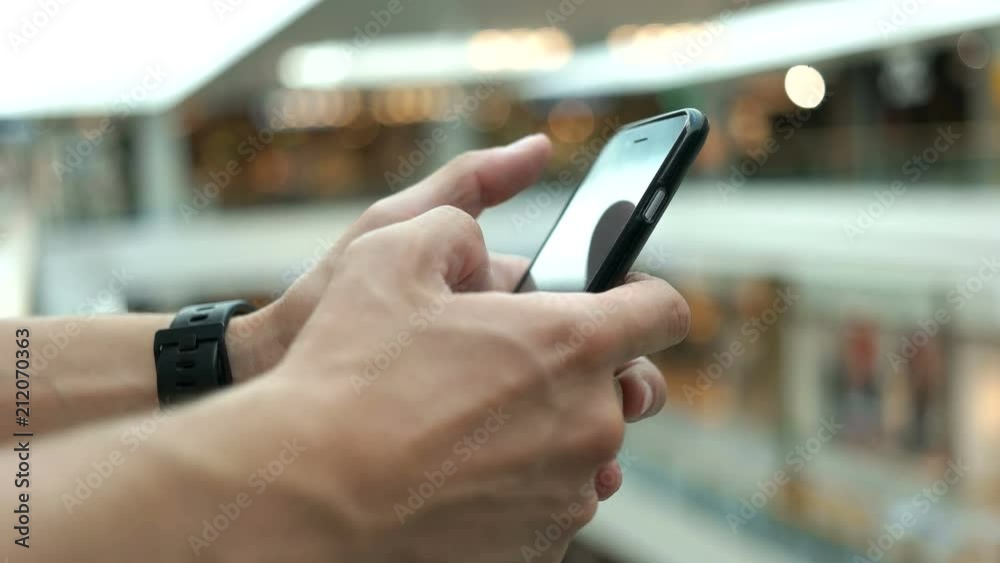 Close up shot of young man using smart phone for chatting with friends on the shopping centre background.