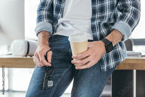 cropped shot of man holding eyeglasses and coffee to go