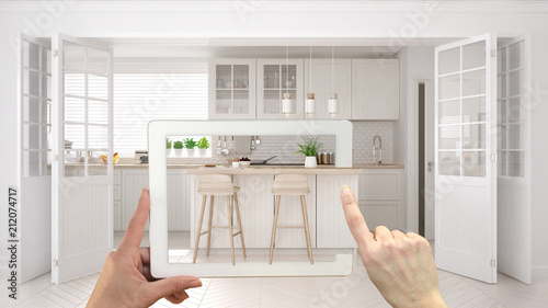 Augmented reality concept. Hand holding tablet with AR application used to simulate furniture and interior design products in real home, scandinavian kitchen with island
