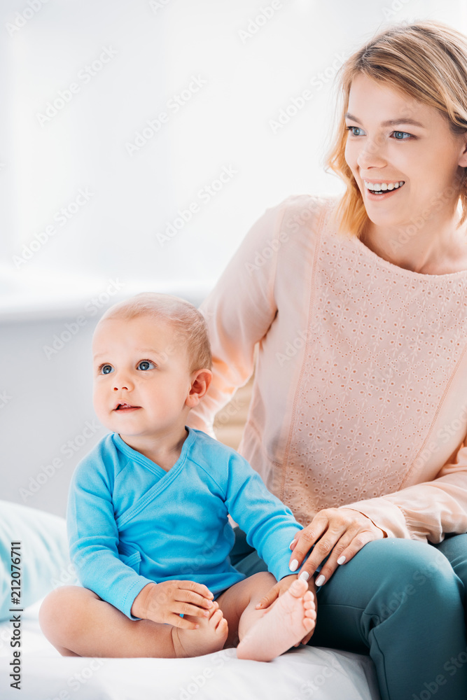 happy mother and child sitting on bed at home and looking away happy mother and child sitting on bed at home and looking away
