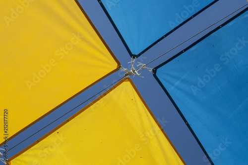 fondo con lona de dos colores/Toldos decorativos de dos colores amarillo y azul formando una x en verano en una calle de Madrid. España