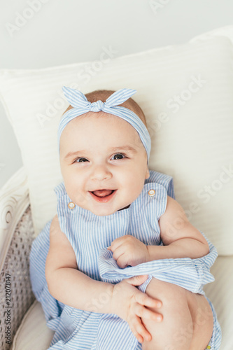 Cute smiling baby girl on white studio backgroung. 6 months baby in blue dress with big smile