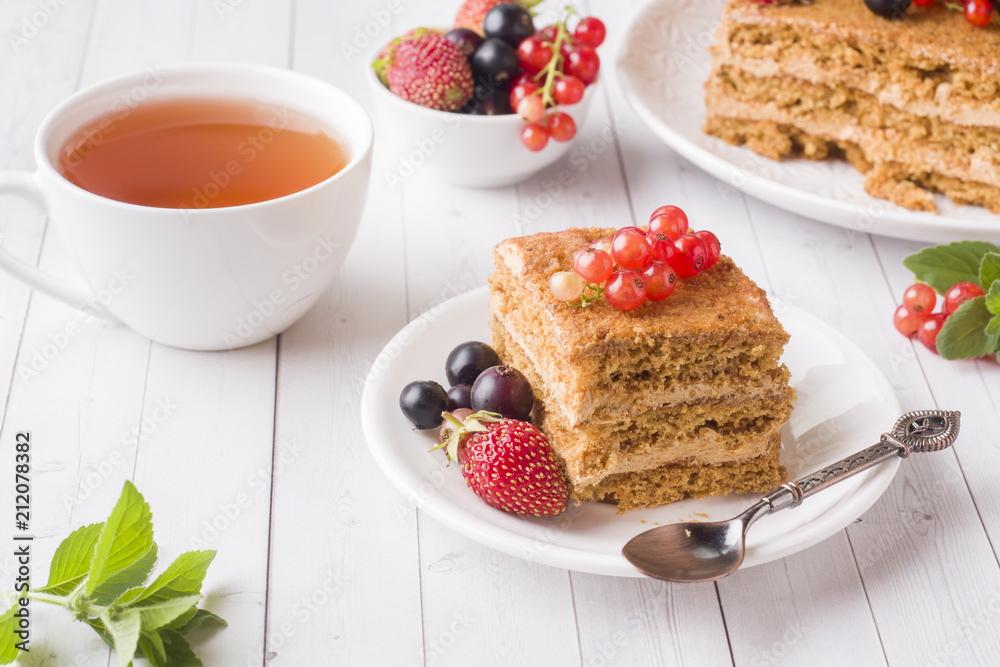 Honey cake with strawberries, mint and currant, a Cup of tea on a light background Honey cake with strawberries, mint and currant, a Cup of tea on a light background