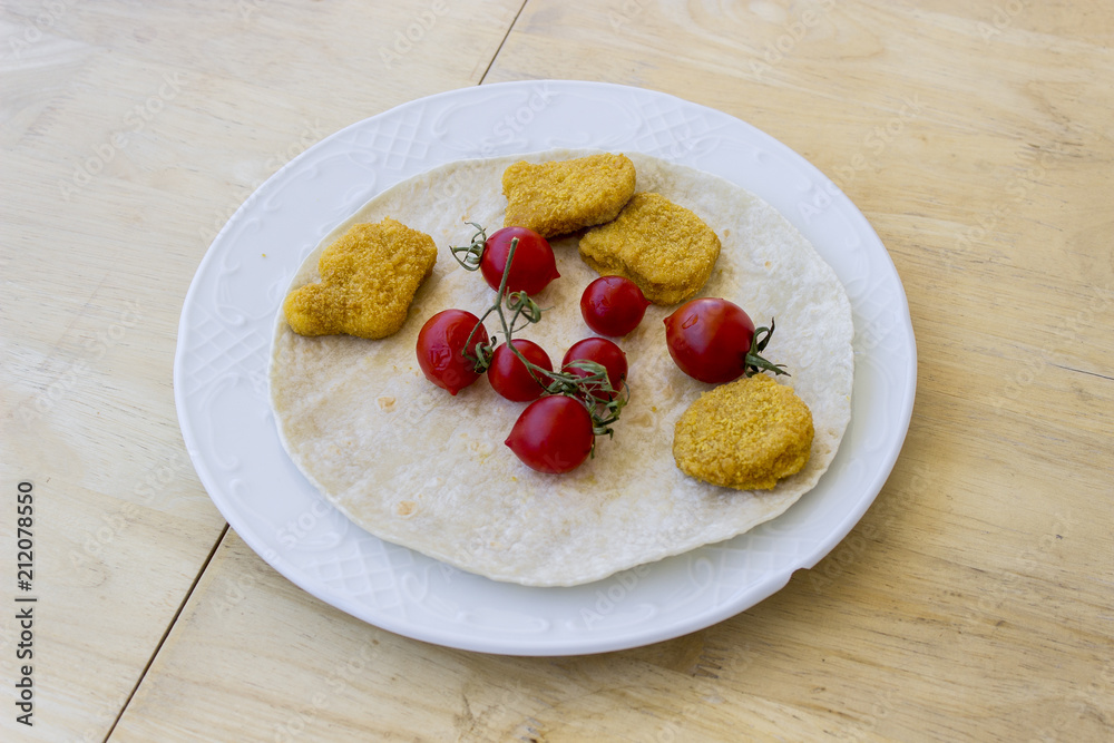 Perspective shot of chicken nuggets and small red fresh tomatoes on the wide white plate as a breakfast with thin bread on center Perspective shot of chicken nuggets and small red fresh tomatoes on the wide white plate as a breakfast with thin bread on center