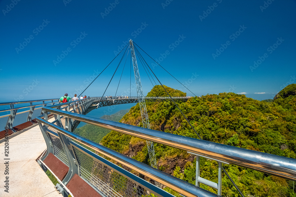 Tourists walking on the Langkawi Sky Bridge, a curved pedestrian cable-stayed bridge, suspended by cables from a single pylon, at the peak of Gunung Mat Chinchang on Langkawi Island, Kedah, Malaysia. Tourists walking on the Langkawi Sky Bridge, a curved pedestrian cable-stayed bridge, suspended by cables from a single pylon, at the peak of Gunung Mat Chinchang on Langkawi Island, Kedah, Malaysia.