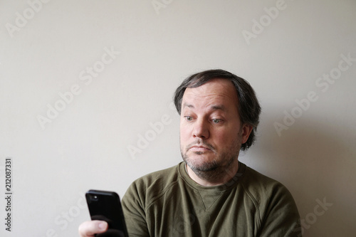 wide-eyed man looking at smartphone, sitting by wall with copy space © Axel Bueckert