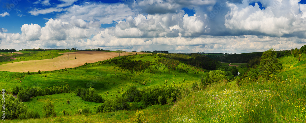 Rural landscape with fields, waves and blue sky with clouds, spring seasonal natural background