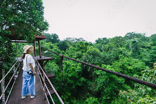 Asian woman walking on canopy walkway with rain forest in Thung Khai Botanical Garden, Trang province, Thailand.