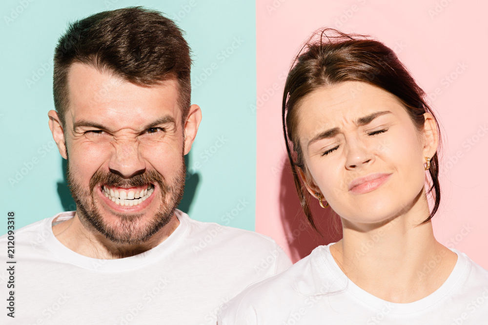 Closeup portrait of young couple, man, woman. One being excited happy smiling, other serious, concerned, unhappy on pink and blue background. Emotion contrasts Closeup portrait of young couple, man, woman. One being excited happy smiling, other serious, concerned, unhappy on pink and blue background. Emotion contrasts
