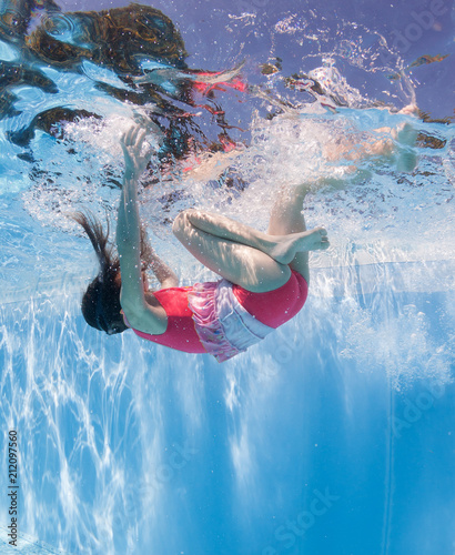 Sporty little girl in a striped swimsuit swims underwater in the pool near the bottom. Underwater photography.