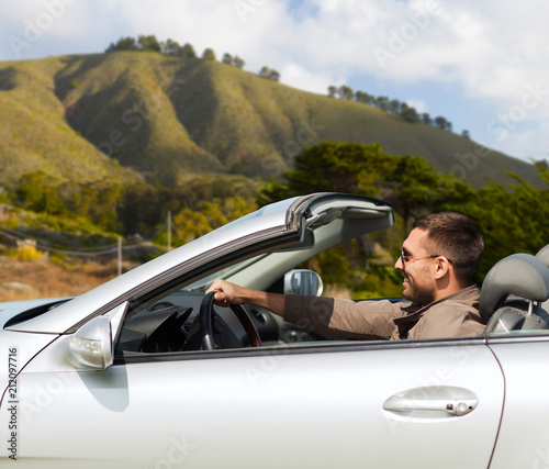 road trip, travel and people concept - happy man driving convertible car over big sur hills background in california