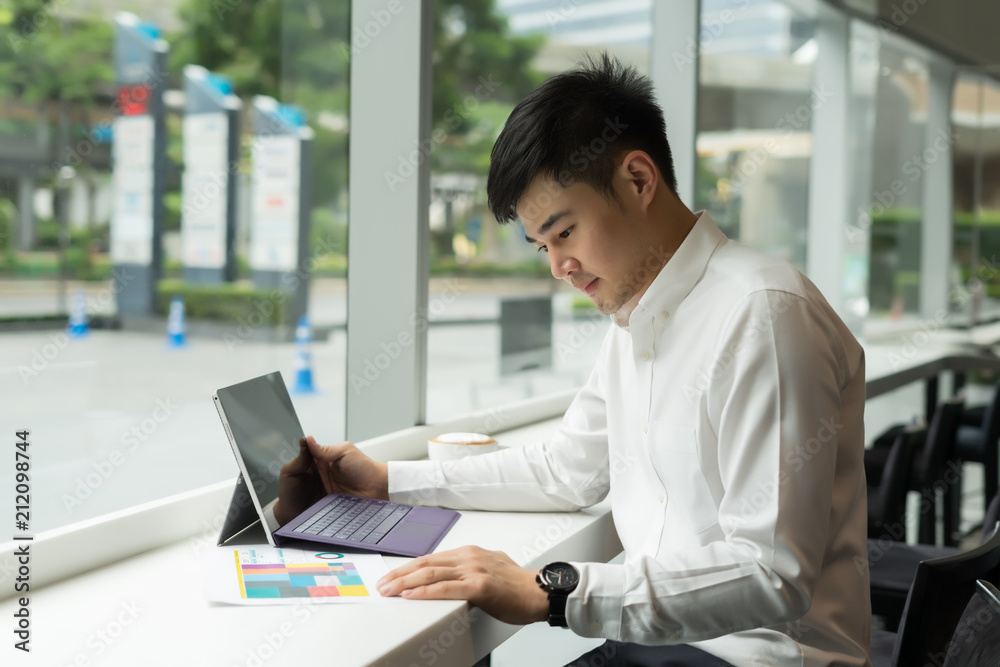 Handsome Asia businessman using laptop and analysis graph visualization at coffee shop