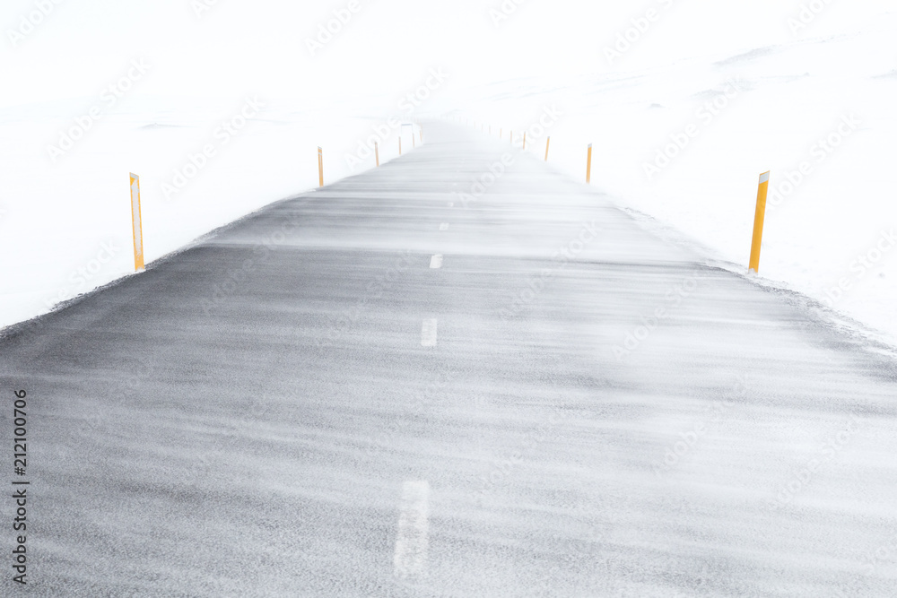 High  wind blowing snow flurry across an empty road in a snowy landscape