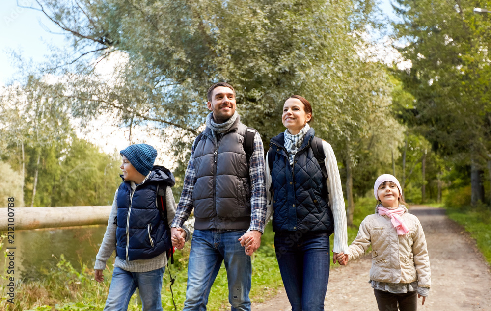 family, tourism and hiking concept - happy mother, father, son and daughter with backpacks walking in woods