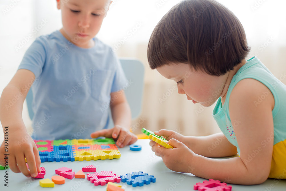 Fototapeta premium A boy and a girl collect a soft puzzle at the table. Brother and sister have fun playing together in the room. Preschool children and educational toys