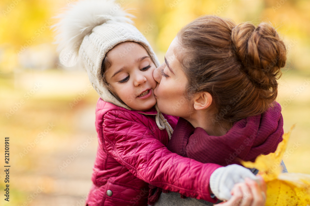 family, love and people concept - happy mother kissing her little daughter in autumn family, love and people concept - happy mother kissing her little daughter in autumn
