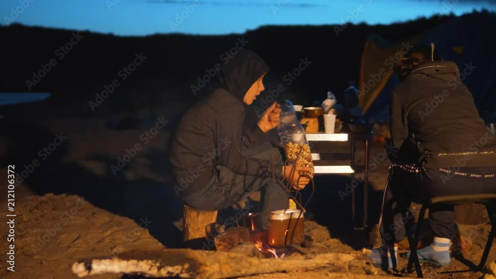 children silhouette kids teen sit by the fire eating popcorn at night campfire. travel hiking adventure camping adventure camping. tourists are warming themselves by the fire. kids hikers concept children silhouette kids teen sit by the fire eating popcorn at night campfire. travel hiking adventure camping adventure camping. tourists are warming themselves by the fire. kids hikers concept