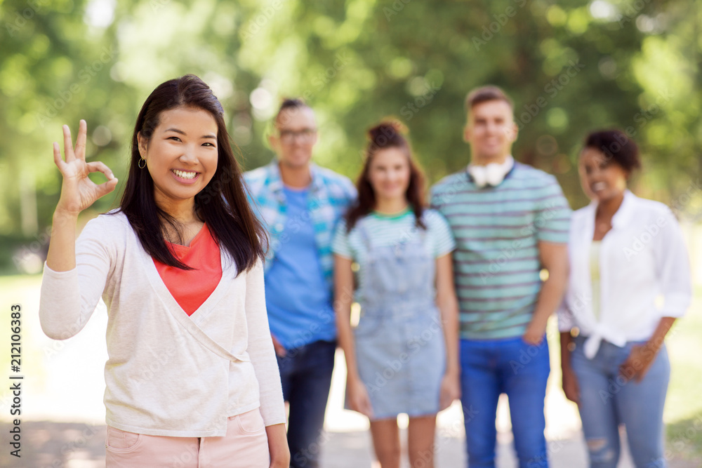 people, friendship and international concept - happy smiling asian woman showing ok hand sign and group of happy friends outdoors people, friendship and international concept - happy smiling asian woman showing ok hand sign and group of happy friends outdoors