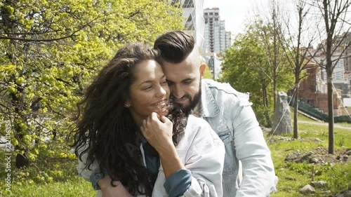 Beautiful romantic young couple outdoor with the young man hugging his girlfriend or wife as she smile in enjoyment, wearing denim jackets, slow motion