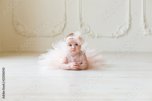 Baby girl wearing a peach tutu. Cute smiling baby girl lying on the floor on creamy background