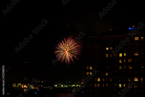 A Fourth of July fireworks display explodes over the waterfront in the city center of Norfolk Virginia, in the context of buildings, apartments, and dwellings