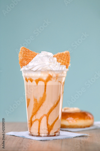Delicious fresh milk and ice cream with whipped cream and cookie in glass on table with cheesecake on blue background