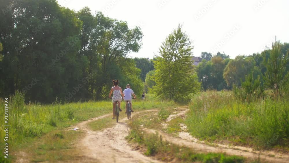 Rear view of young couple cycling on country road at summer day Rear view of young couple cycling on country road at summer day