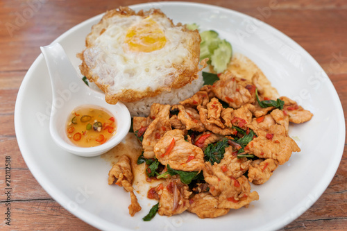 Thai street food on white dish with fried egg and fish sauce "Kao Pad Kapao Moo" ,It's cooked from  pork , sweet basil and chili.