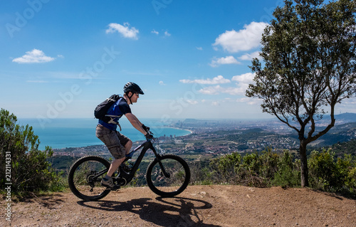 Scenic view of male mountain biker on an electric bike with Barcelona City in the background