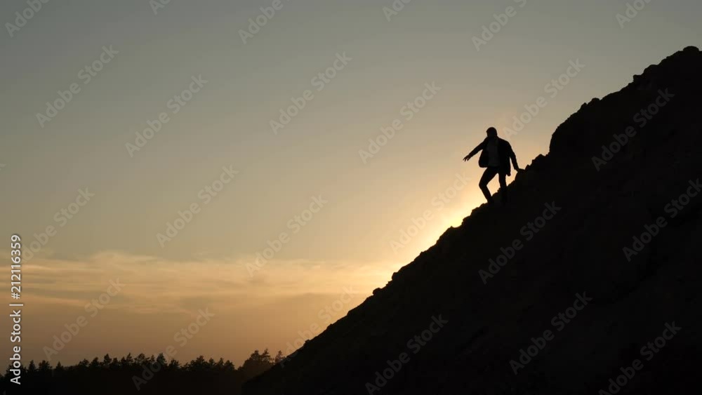 Silhouette of a man coming down from a steep mountainside at sunset Silhouette of a man coming down from a steep mountainside at sunset