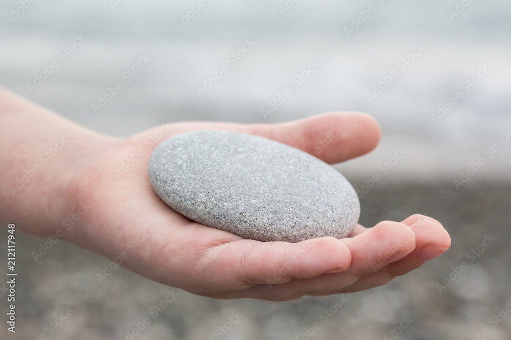 A child holds a pebble in his hand - obrazy, fototapety, plakaty 