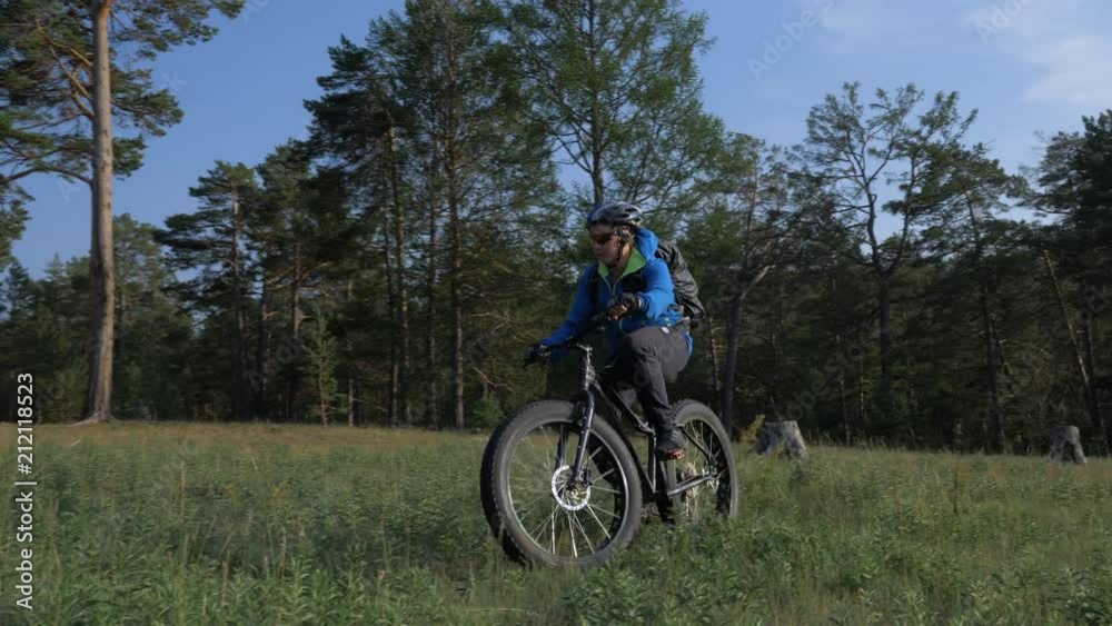 Fat bike also called fatbike or fat-tire bike in summer riding in the forest. The guy rides a bicycle among trees and stumps. He overcomes some obstacles on a bumpy road. Fat bike also called fatbike or fat-tire bike in summer riding in the forest. The guy rides a bicycle among trees and stumps. He overcomes some obstacles on a bumpy road.