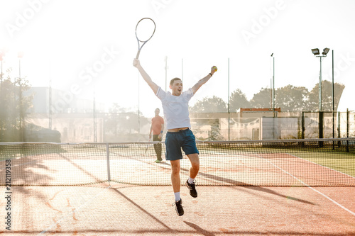Front view of happy young man in polo shirt holding tennis racket