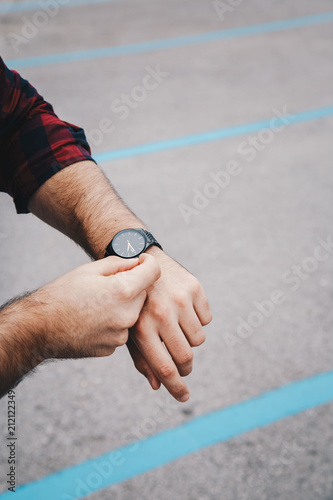 close up fashion details, young fashionable man wearing a red checked shirt and a black analog wrist watch. street style detail of an elegant clock.